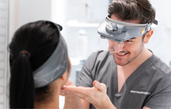 A skincare professional examines a client's face under a magnifying headlamp.